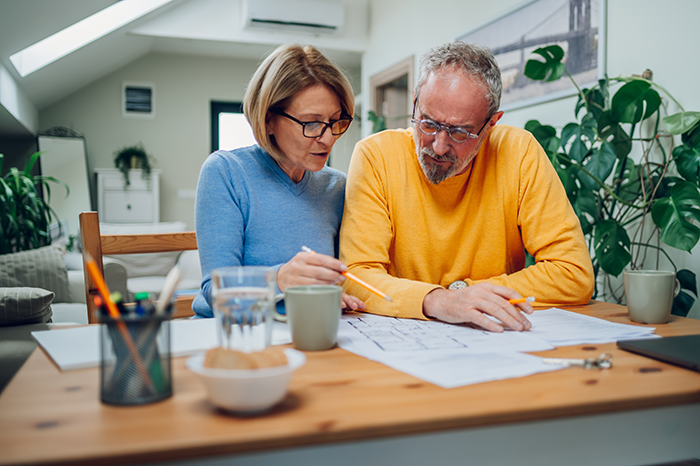 Older couple reviewing paperwork together at a kitchen table, representing home financing, real estate planning, or mortgage documents.